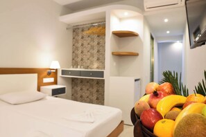 A hotel room with a bed, a bedside table, a lamp, a small cabinet, and a fruit bowl on the side. - Tsampika Hotel (Rhodes)
