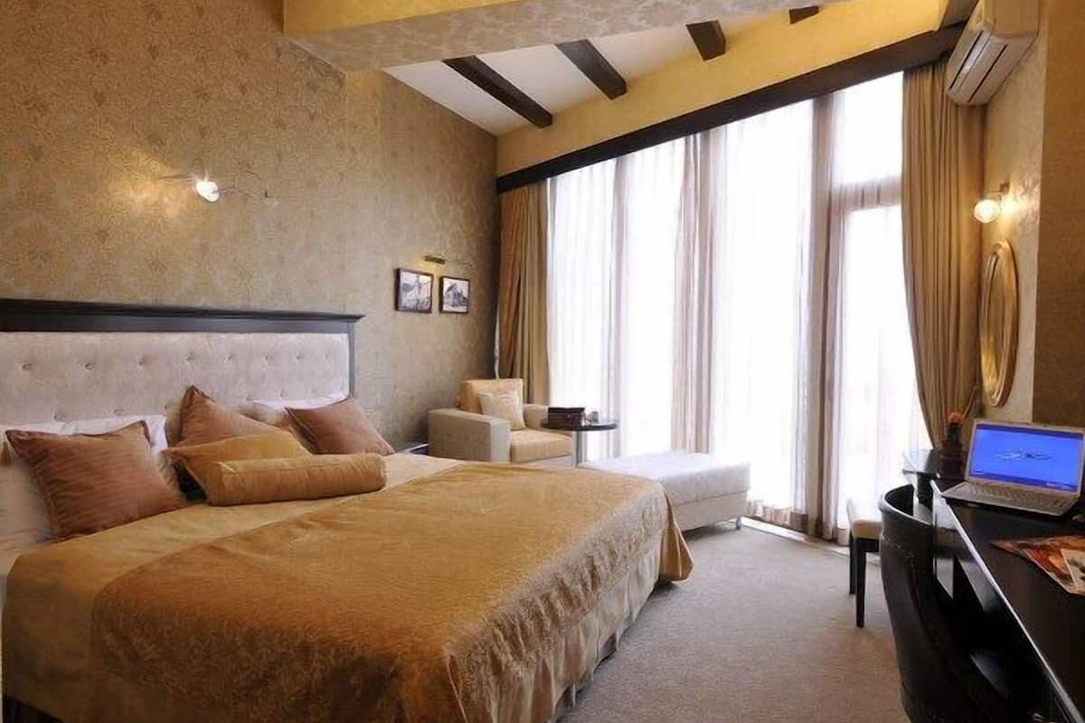 Una camera d'albergo con un letto grande, una scrivania con un portatile, una sedia e un divano.