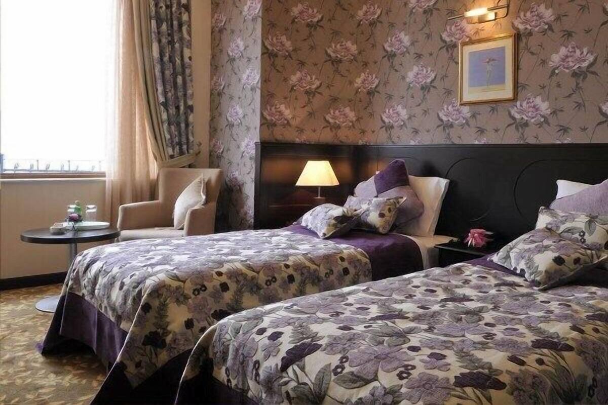 Una camera d'albergo con due letti, una sedia, un tavolino e una lampada.