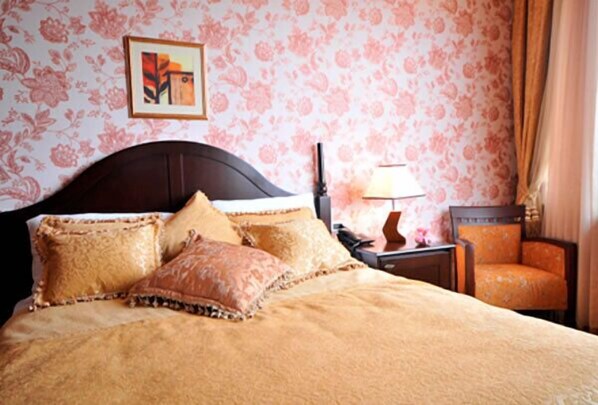 A hotel room with a large bed, a nightstand, a lamp, and a chair. - Riviera Hotel (Baku)