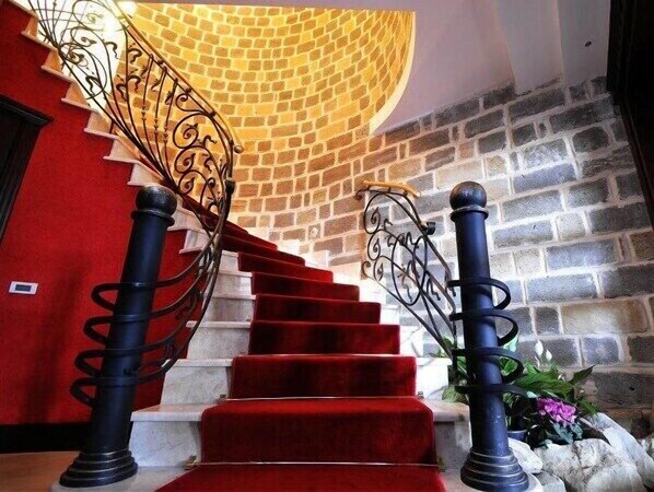 A staircase with red carpeted steps, black balusters, and a curved wall with a brick pattern. - Riviera Hotel (Baku)