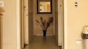 A hallway with a mirror, a potted plant, and a trash bin. - Pousada dos Franceses (São Paulo)