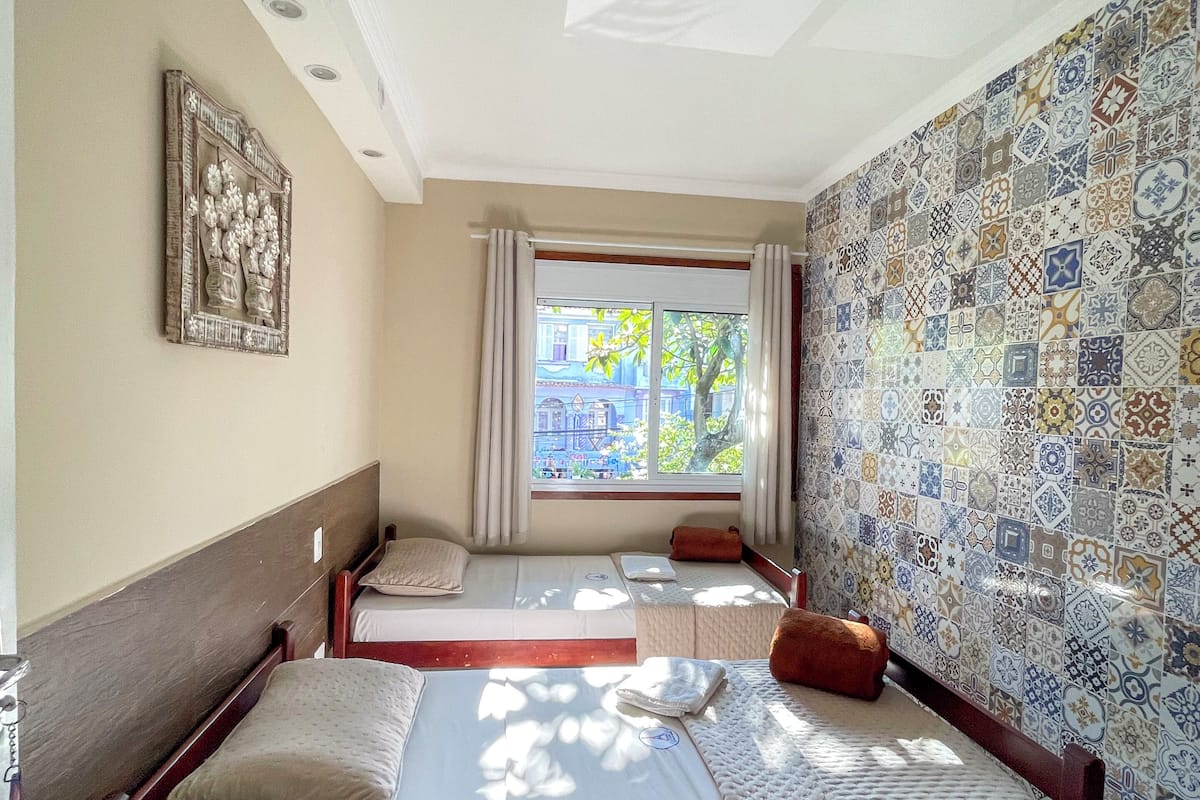 A room with two beds, a window with curtains, a patterned wall, and a ceiling with recessed lighting.