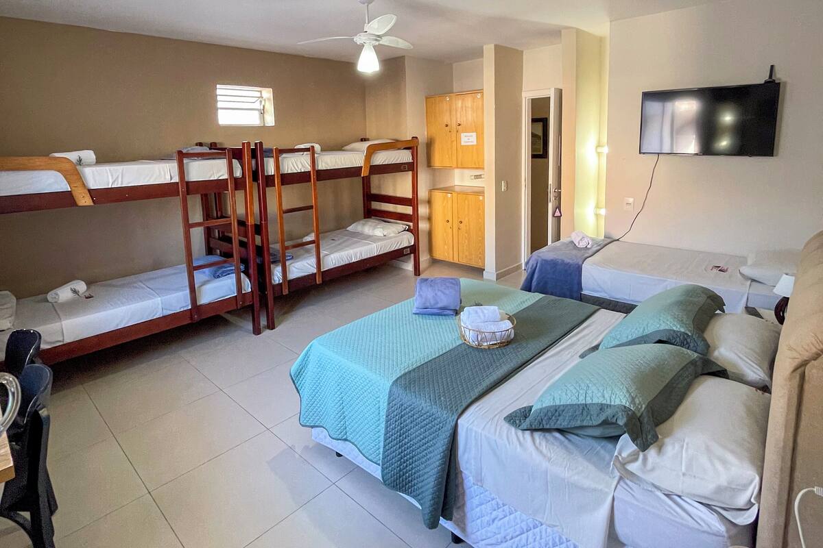 A dormitory-style room with bunk beds, a ceiling fan, a television, and a desk with a chair.