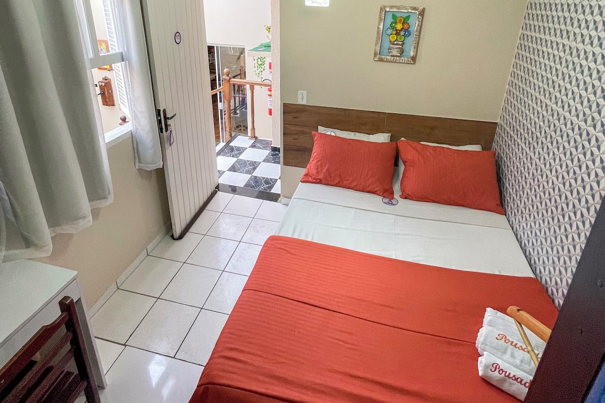 A hotel room with a bed, a desk, a chair, a wardrobe, and a door leading to a balcony.