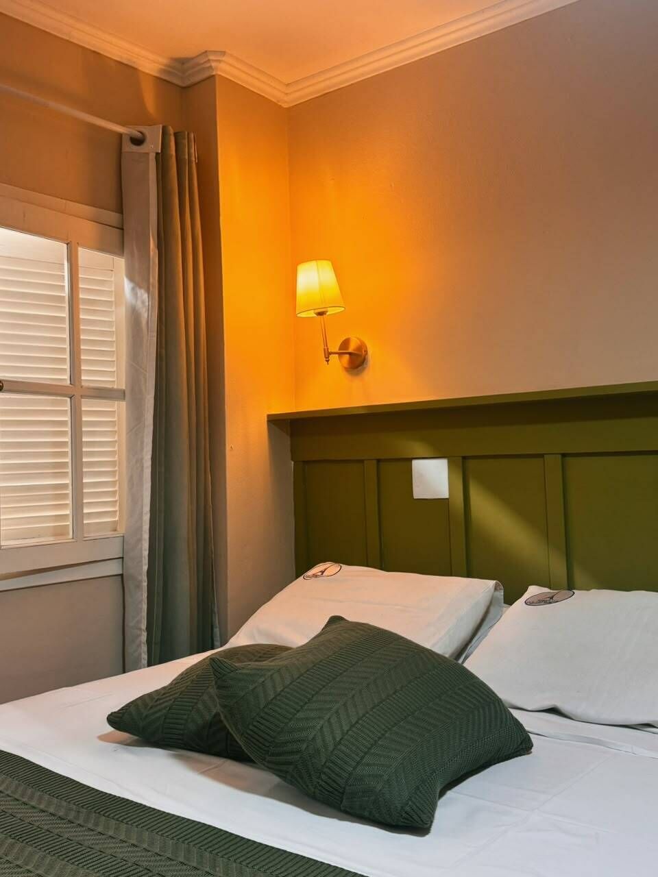 Een hotelkamer met een bed, een nachtkastje, een lamp en een raam met gordijnen.