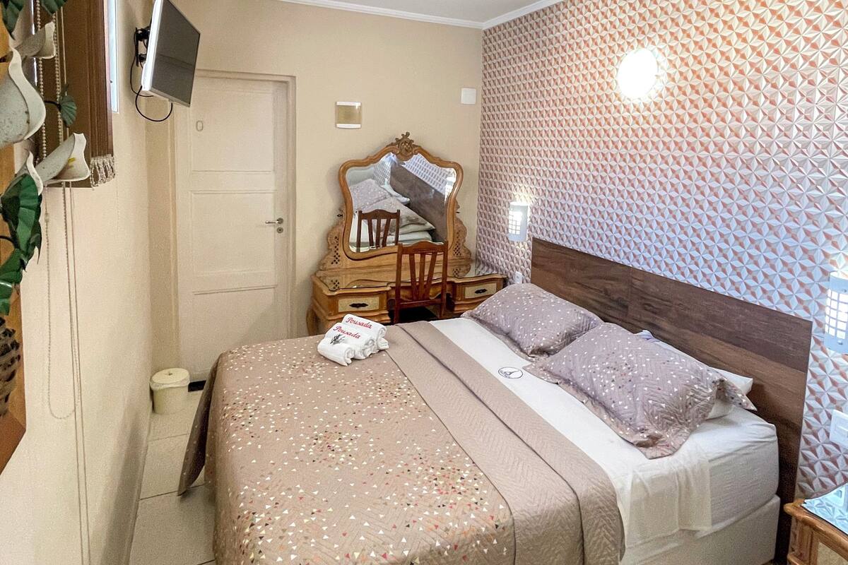 A neatly arranged bedroom with a bed, bedside tables, a mirror, and a wall with a geometric pattern.