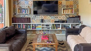 A living room with a patterned wall, a flat-screen TV, bookshelves, a coffee table, and two sofas. - Pousada dos Franceses (São Paulo)