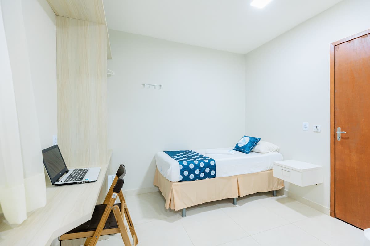 Une chambre à coucher avec un lit, un bureau avec un ordinateur portable, une chaise en bois et une porte en bois.