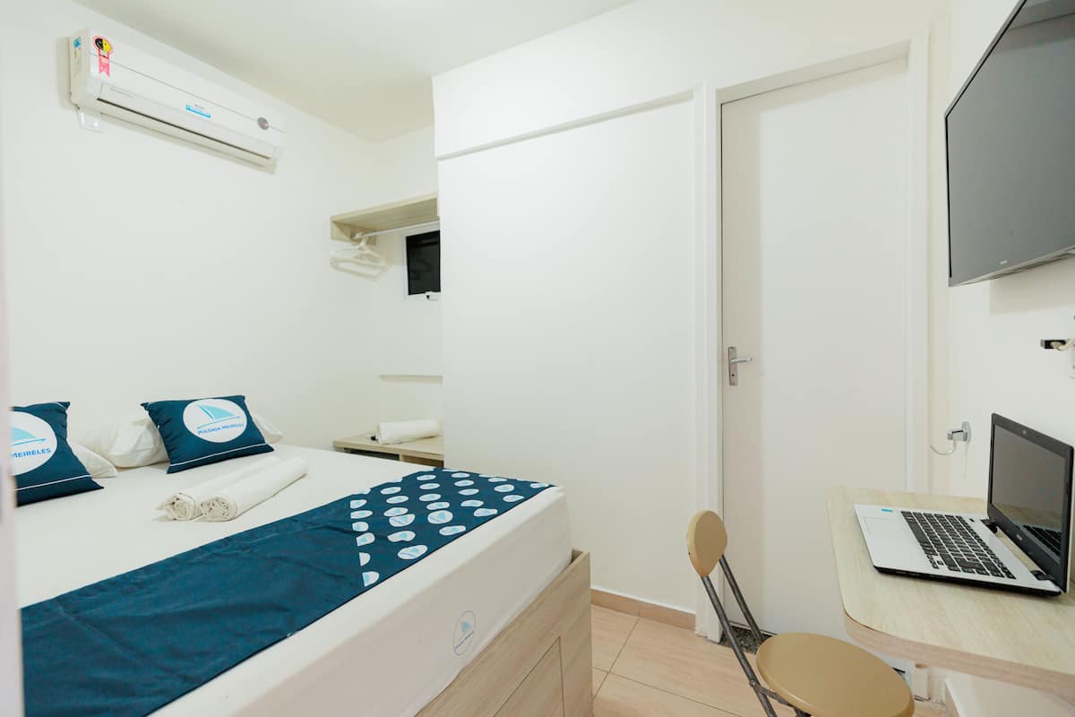 Une chambre d’hôtel équipée d’un lit, d’un bureau avec un ordinateur portable, d’une chaise, d’un climatiseur et d’un téléviseur.