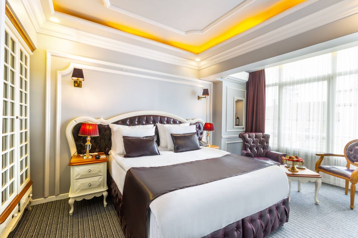 A large, elegantly furnished bedroom with a plush bed, bedside tables, and a seating area with a chair.