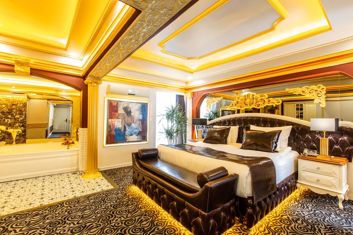 A luxurious bedroom with a large bed, a seating area, a vanity, and a mirror.