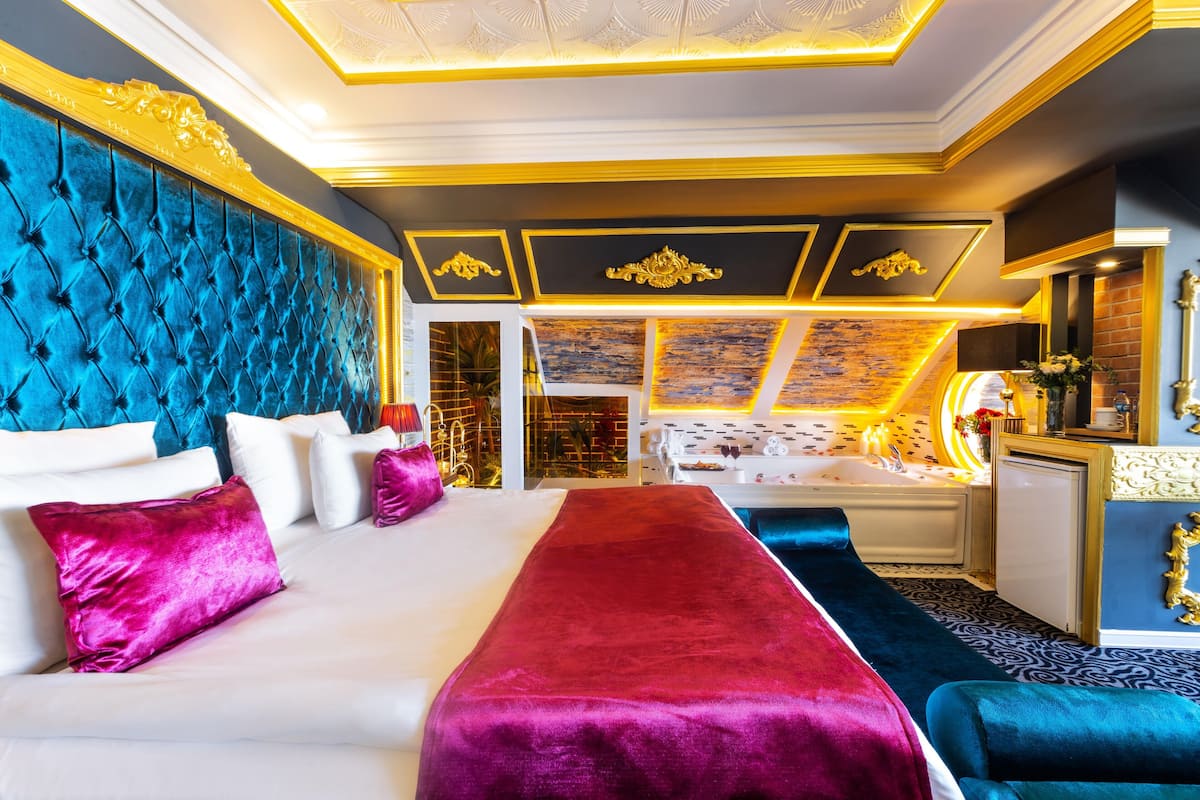 A luxurious hotel room with a large bed, a red and blue accent wall, and a modern bathroom.