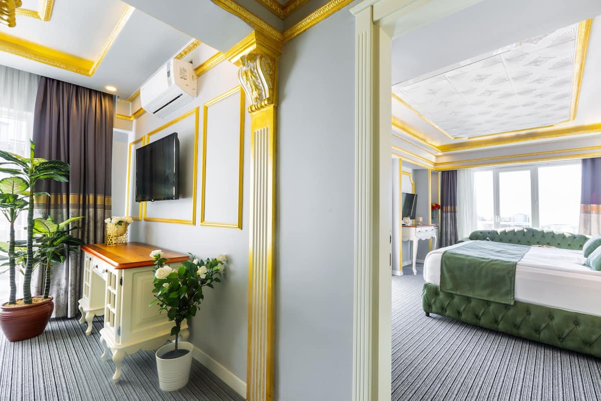 A hotel room with a large bed, a television, a desk with a plant, and a potted plant.