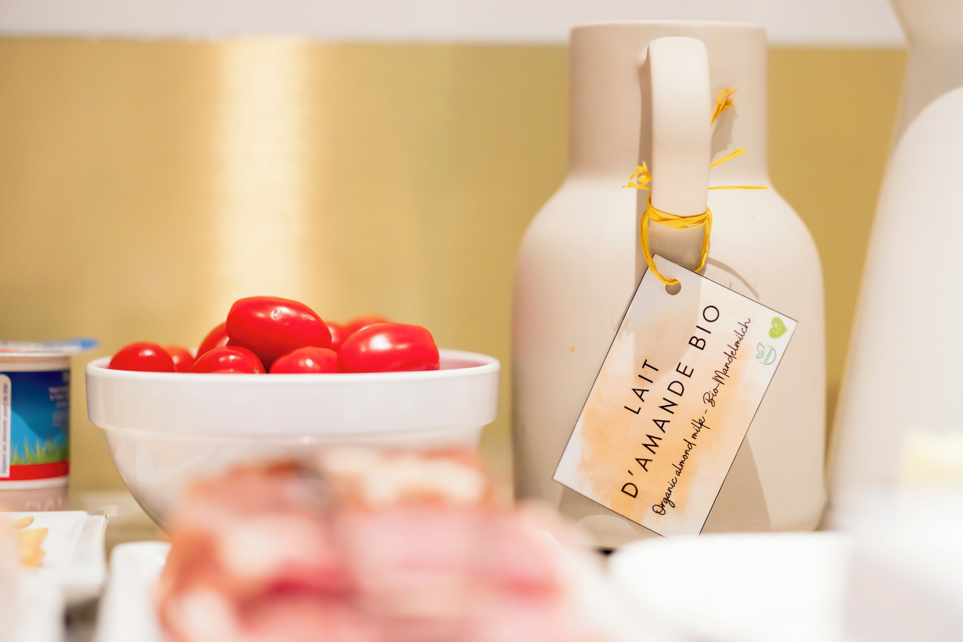 A white bottle with a tag labeled "D'AMANDE BIO" and a bowl of red tomatoes.