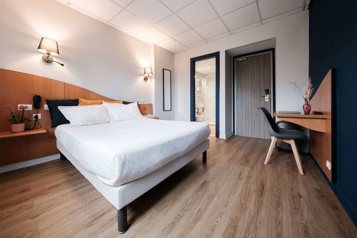 Une chambre d’hôtel moderne, dotée d’un grand lit, de tables de chevet, d’un bureau et d’une chaise.