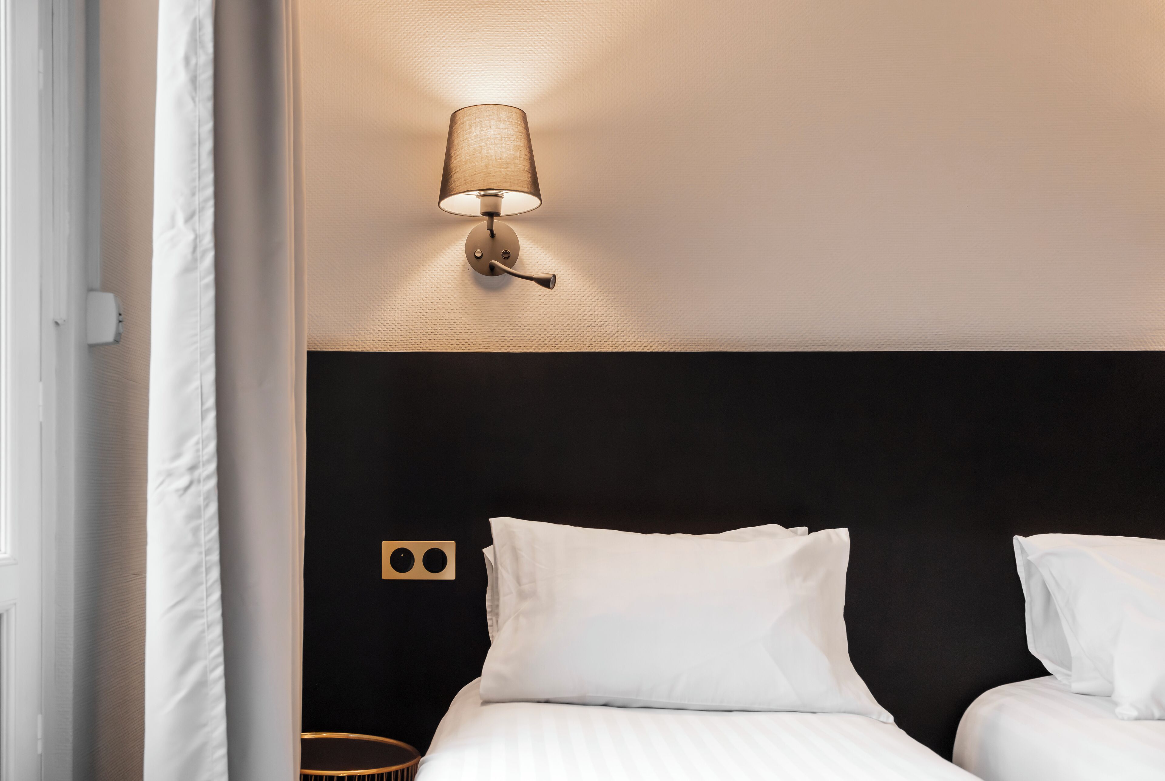 A hotel room with a bed, a wall-mounted lamp, and a small round table.
