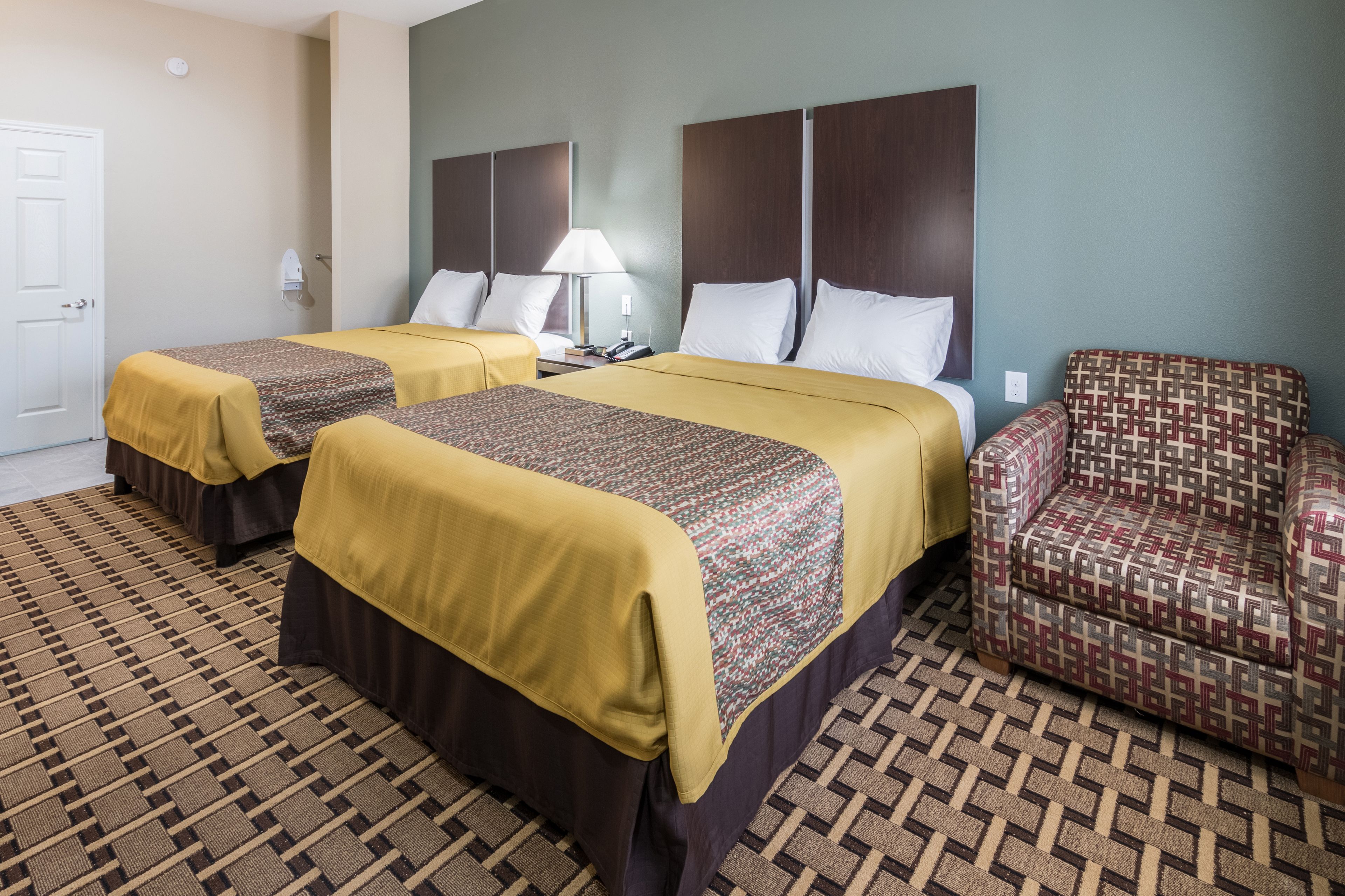 A hotel room with two beds, a sofa, a patterned carpet, and a door.