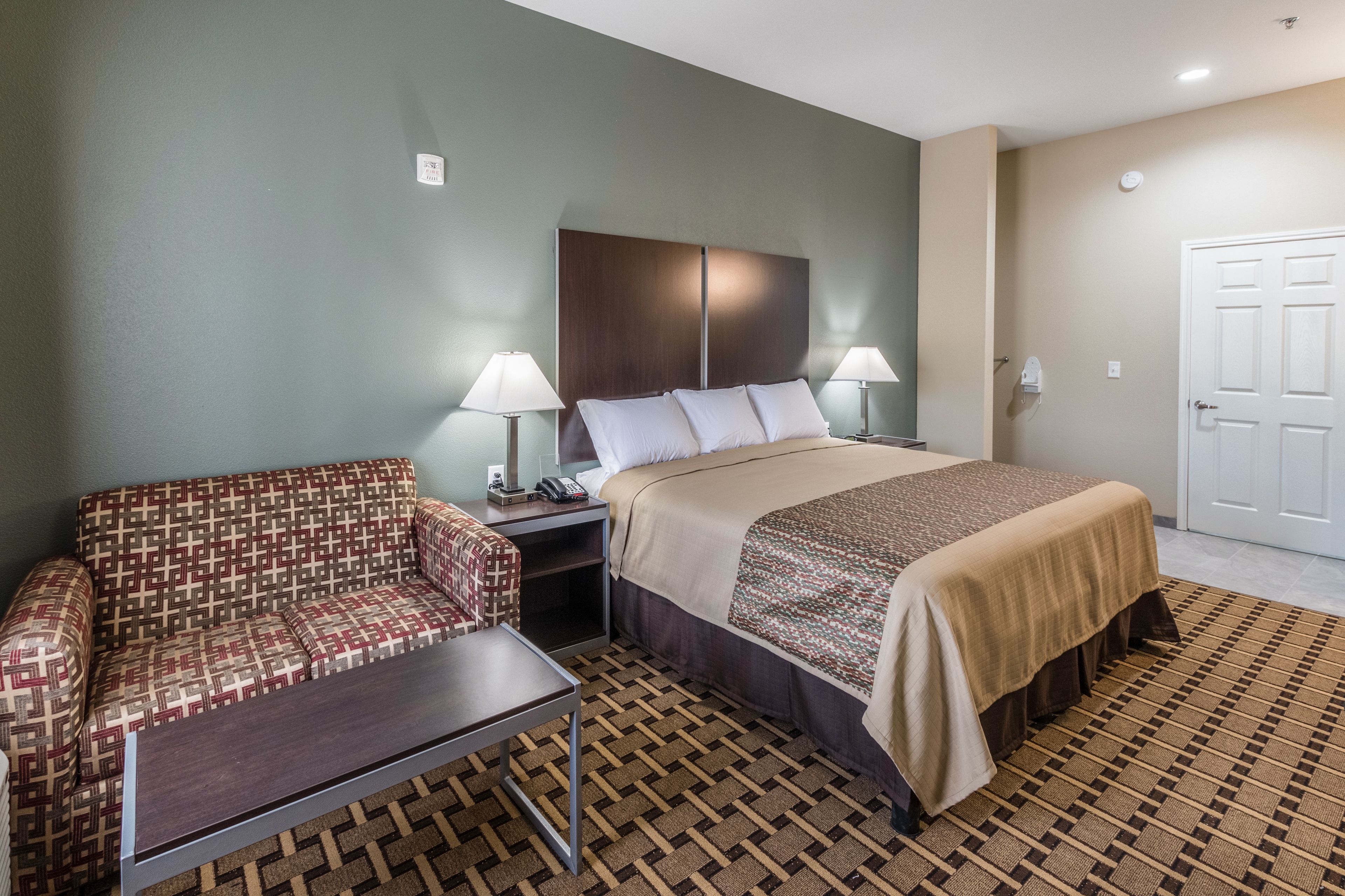 Une chambre d’hôtel avec un lit, un canapé, une table de chevet et une lampe.