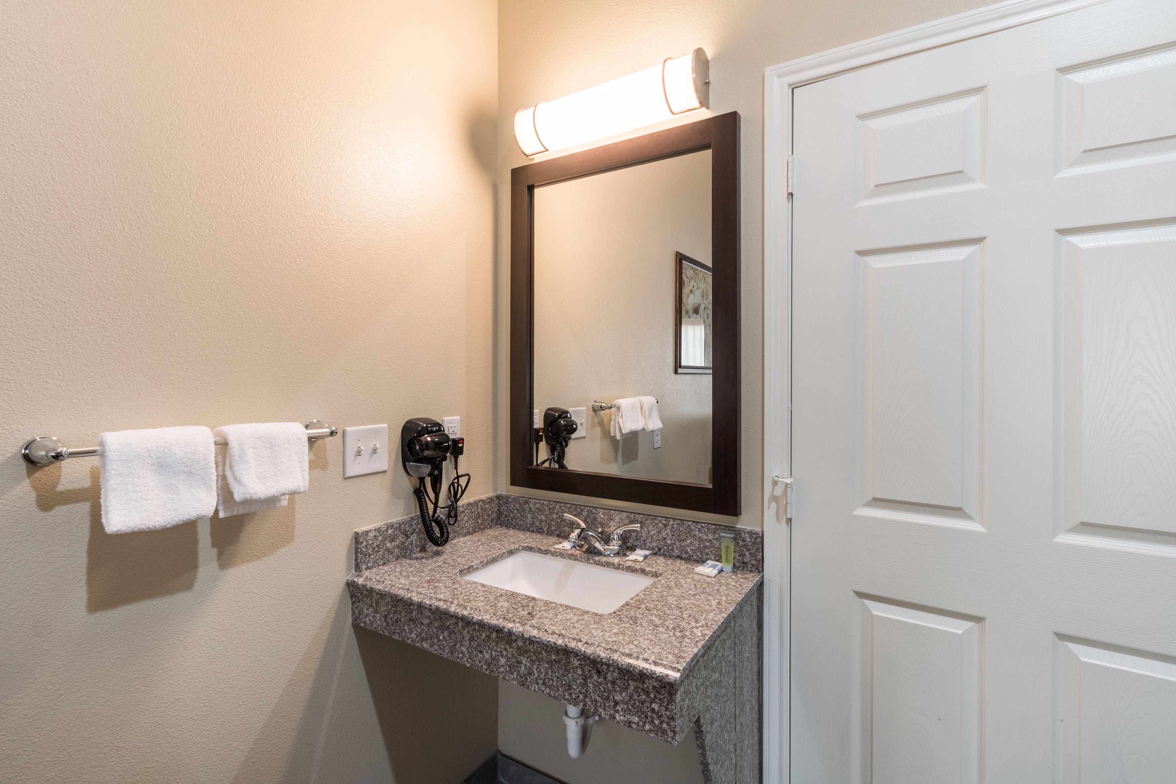 A bathroom with a granite sink, a mirror, a hairdryer, and two towels on a towel rack.