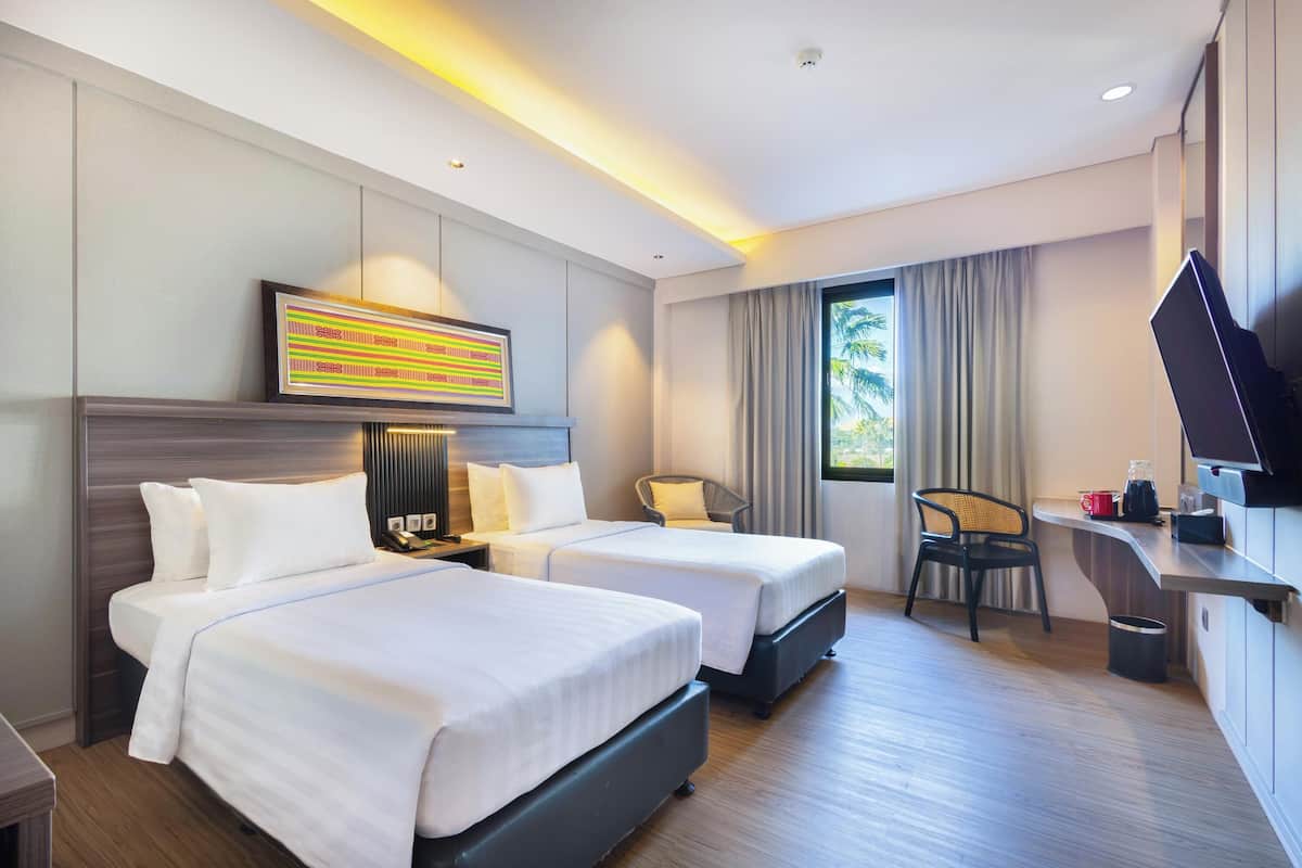 A hotel room with two beds, a desk with a flat-screen TV, a chair, and a window with curtains.