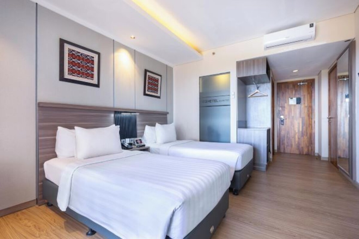 A hotel room with two beds, a minibar, a TV, and a wooden floor.