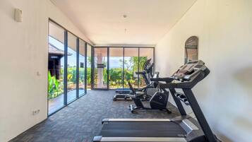 Une salle de sport équipée de tapis de course et d’appareils d’exercice, dotée de grandes fenêtres et offrant une vue sur la verdure.