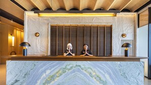 A reception desk with a marble top, two staff members behind a vertical panel, and a ceiling with a wooden design. - Hotel NEO Eltari Kupang by Aston (Kupang)