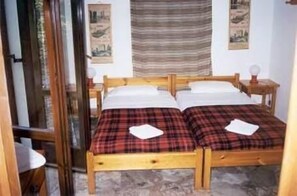 A double bed with plaid bedding, a wooden headboard, and a nightstand with a lamp. - Pension Lagoudera (Naxos)