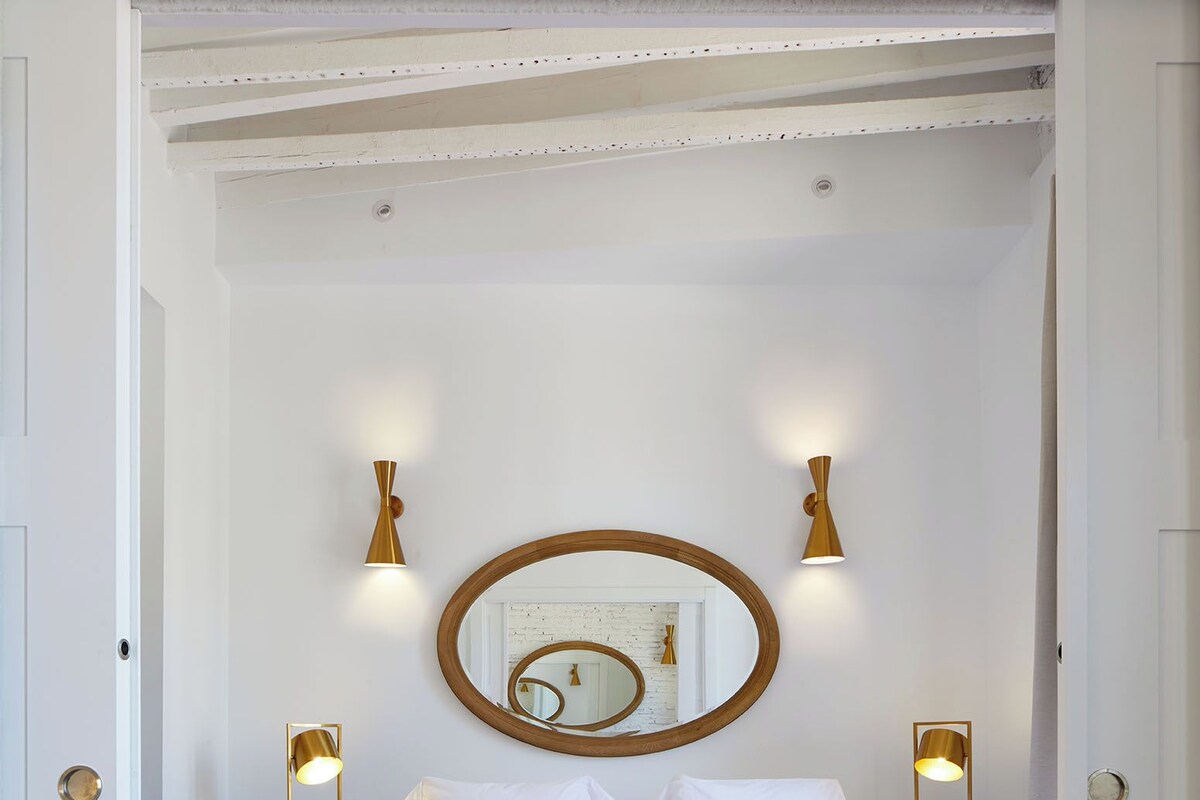 Une chambre d’hôtel avec un grand lit, un miroir, deux tables de chevet avec des lampes et un plaid rouge.