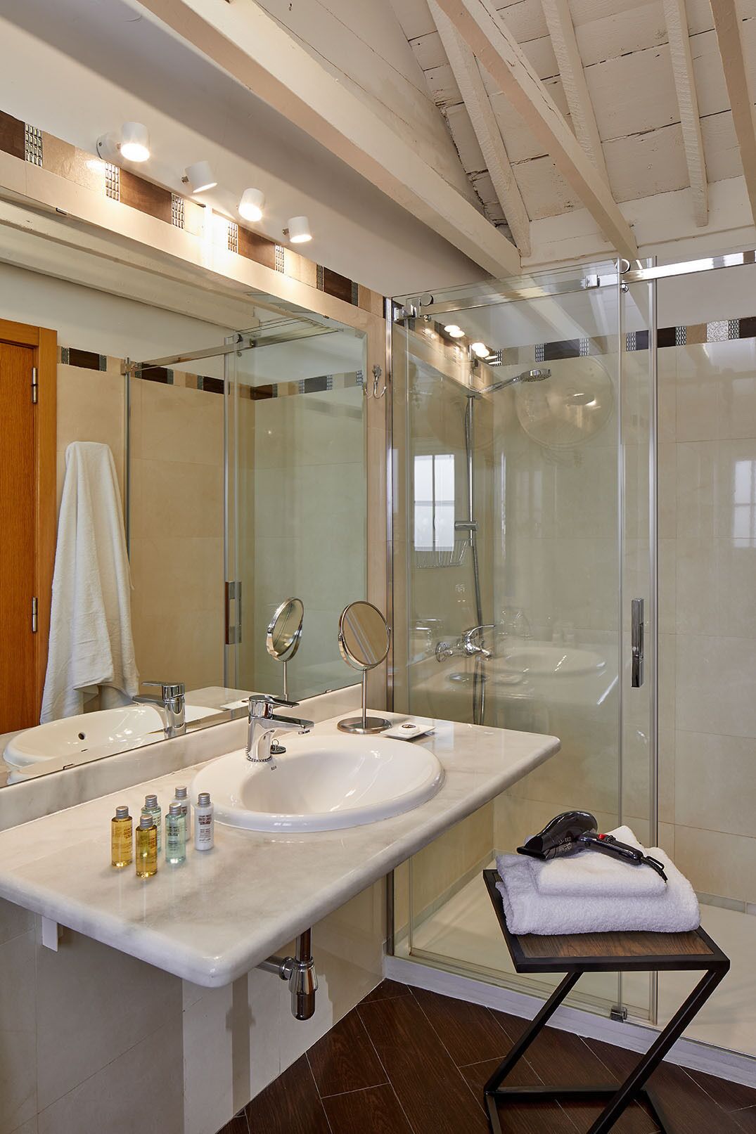 A modern bathroom with a glass-enclosed shower, a large mirror, and a vanity with a sink and toiletries.