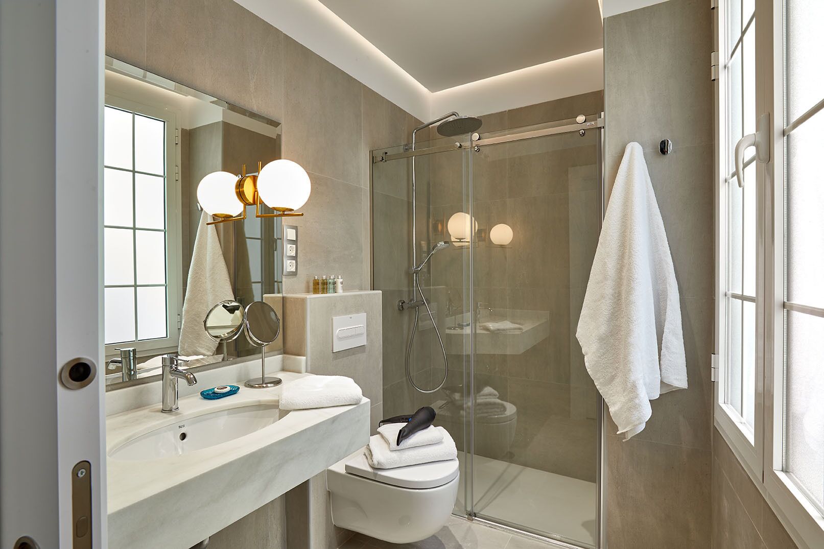 A modern bathroom with a glass-enclosed shower, a large mirror with round lights, and a white sink.
