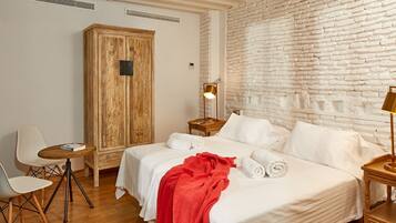 Una habitación de hotel con una cama grande, un armario de madera, un escritorio con lámpara y una pared de ladrillo blanco.