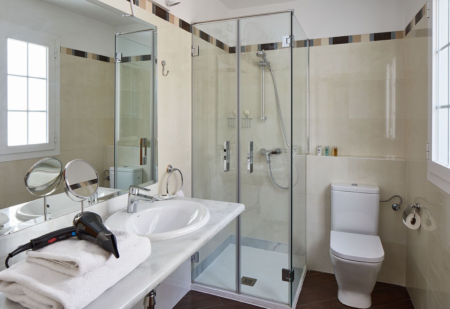 A modern bathroom with a glass-enclosed shower, two sinks with mirrors, and a toilet.