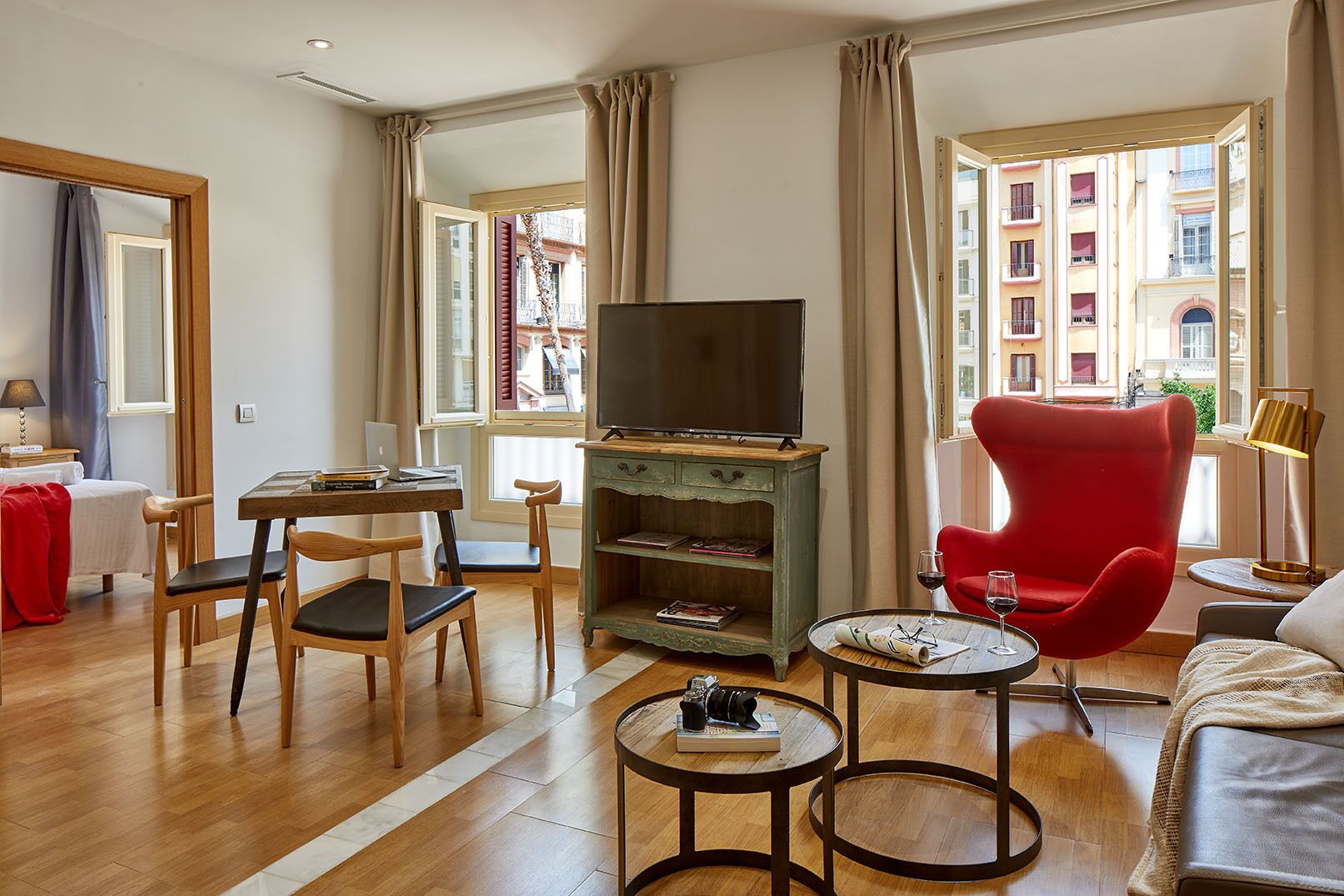 A modern living room with a wooden floor, a red armchair, a television, and a small table with a camera.