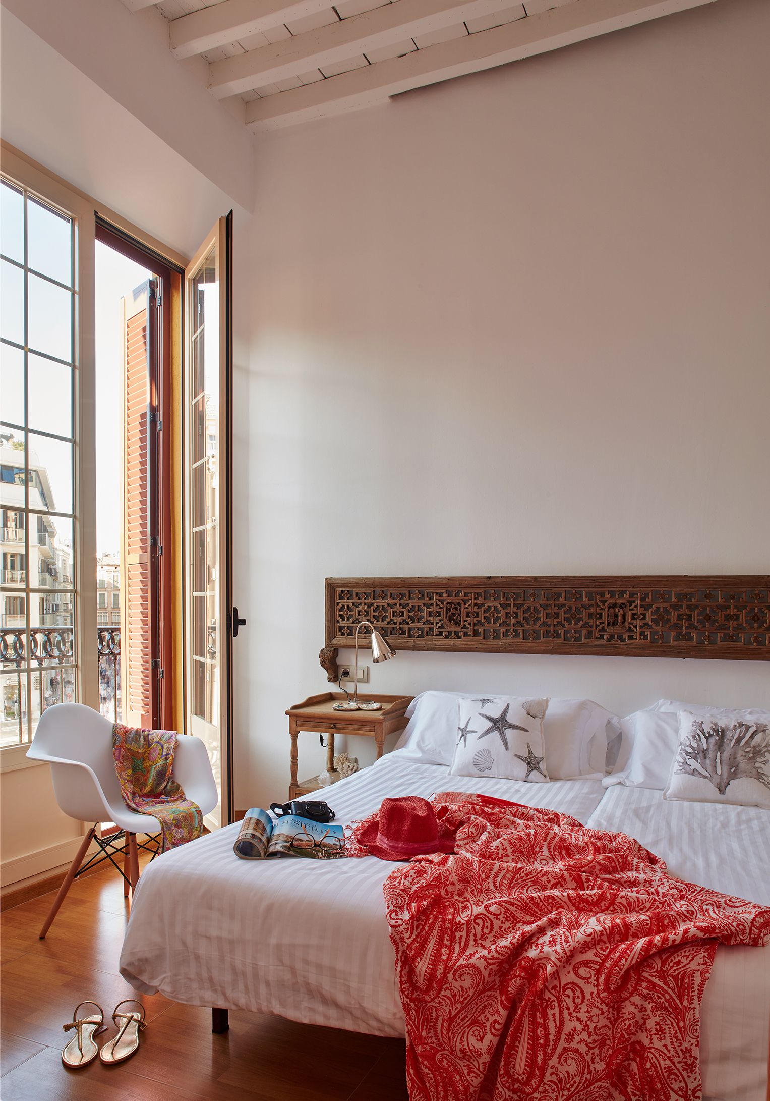 A bedroom with a large bed, a chair, a table, and a view of the city through a large window.