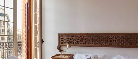 Un dormitorio con una cama grande, una silla, una mesa y vistas a la ciudad a través de un ventanal amplio.