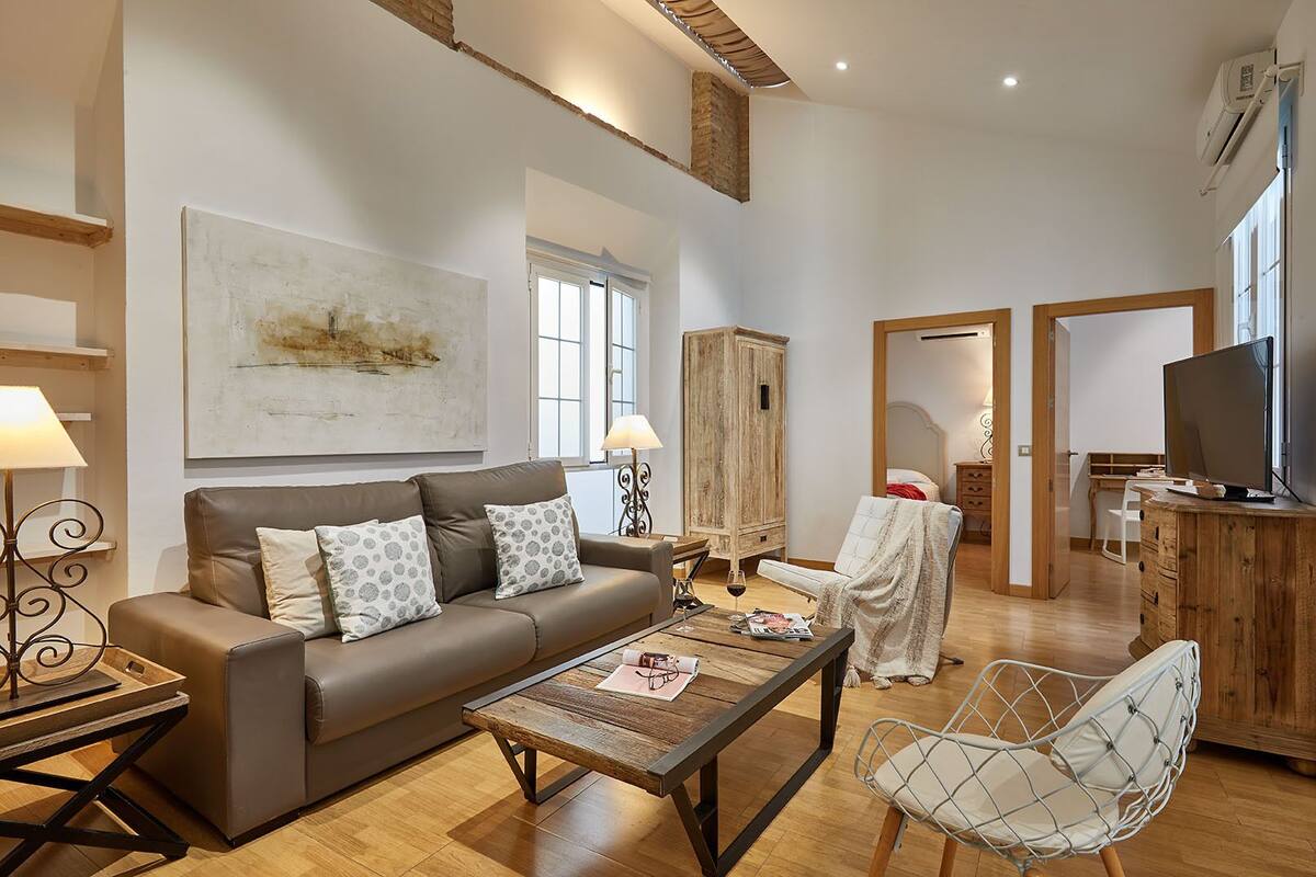Una sala moderna con un sofá, una mesa de centro y un sillón. Hay un mueble de madera, un televisor y una ventana con cortinas.