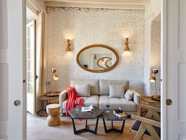 A modern living room with a brick wall, a round mirror, and two floor lamps.