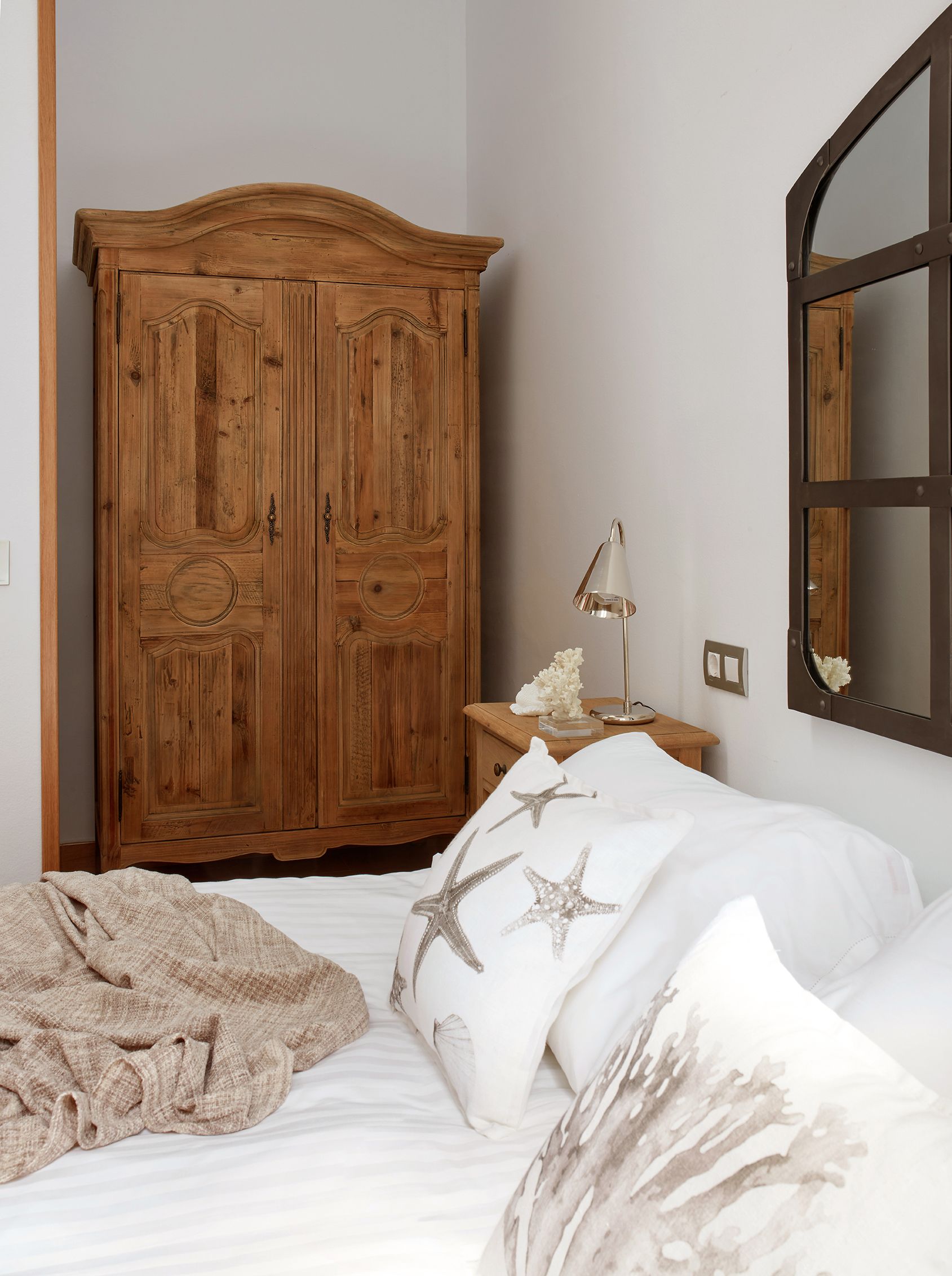 A bedroom with a wooden wardrobe, a bedside table with a lamp, and a bed with starfish pillows.
