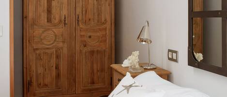 A bedroom with a wooden wardrobe, a bedside table with a lamp, and a bed with starfish pillows.