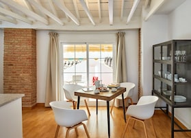 A dining area with a brick wall, a wooden table, white chairs, and a glass cabinet with dishes.