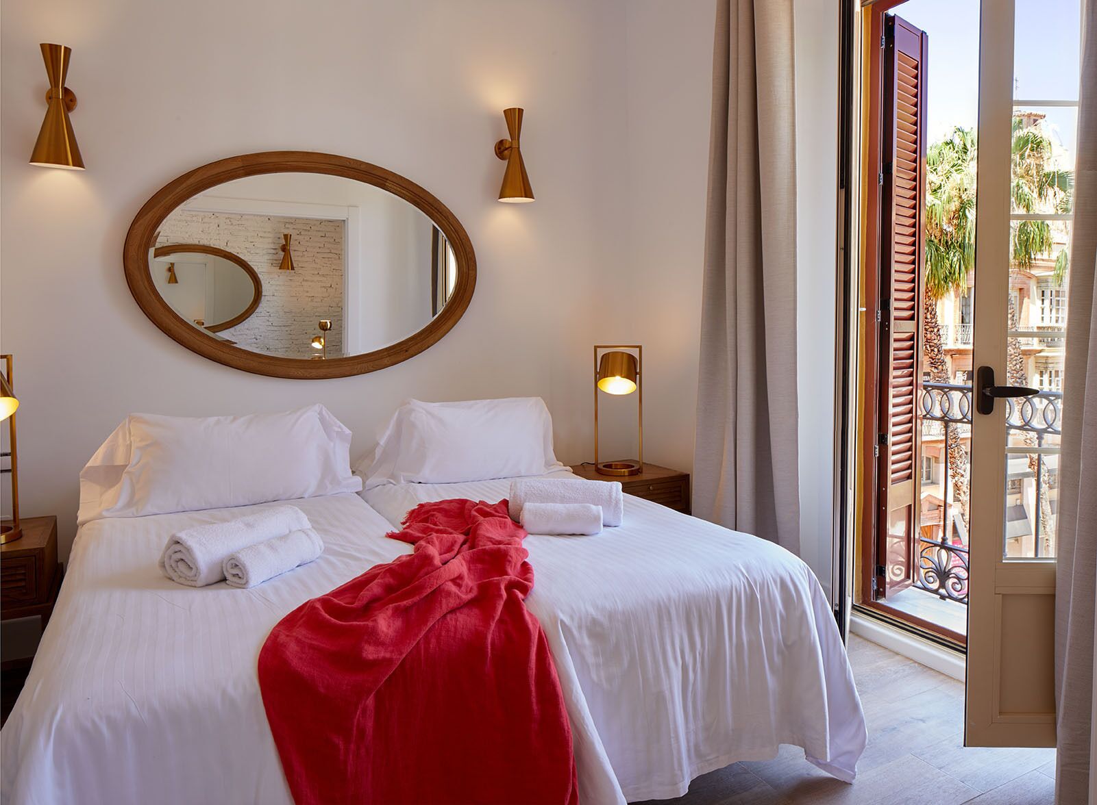 Ein Hotelzimmer mit einem großen Bett, einem runden Spiegel, zwei Nachttischlampen und Blick auf den Balkon.