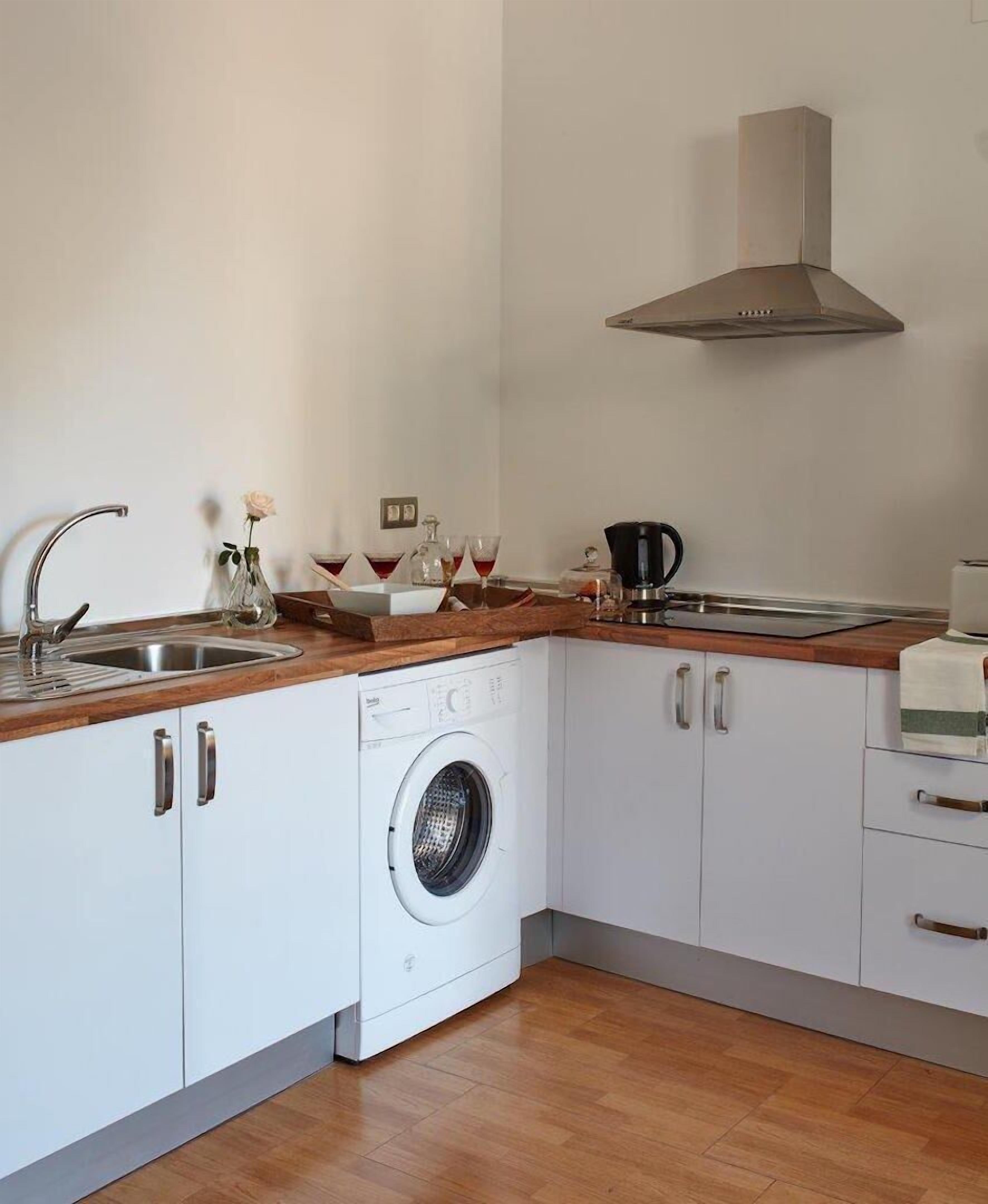 A compact kitchen with a built-in washing machine, stainless steel sink, and a range hood.