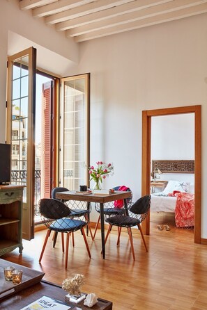 Habitació moderna amb terra de fusta, taula de dinar amb cadirees, televisió i llit amb col·cha estampada.