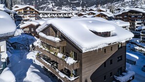 Un hotel de varios pisos con balcones y un tejado cubierto de nieve, rodeado de otros edificios en un paisaje nevado.