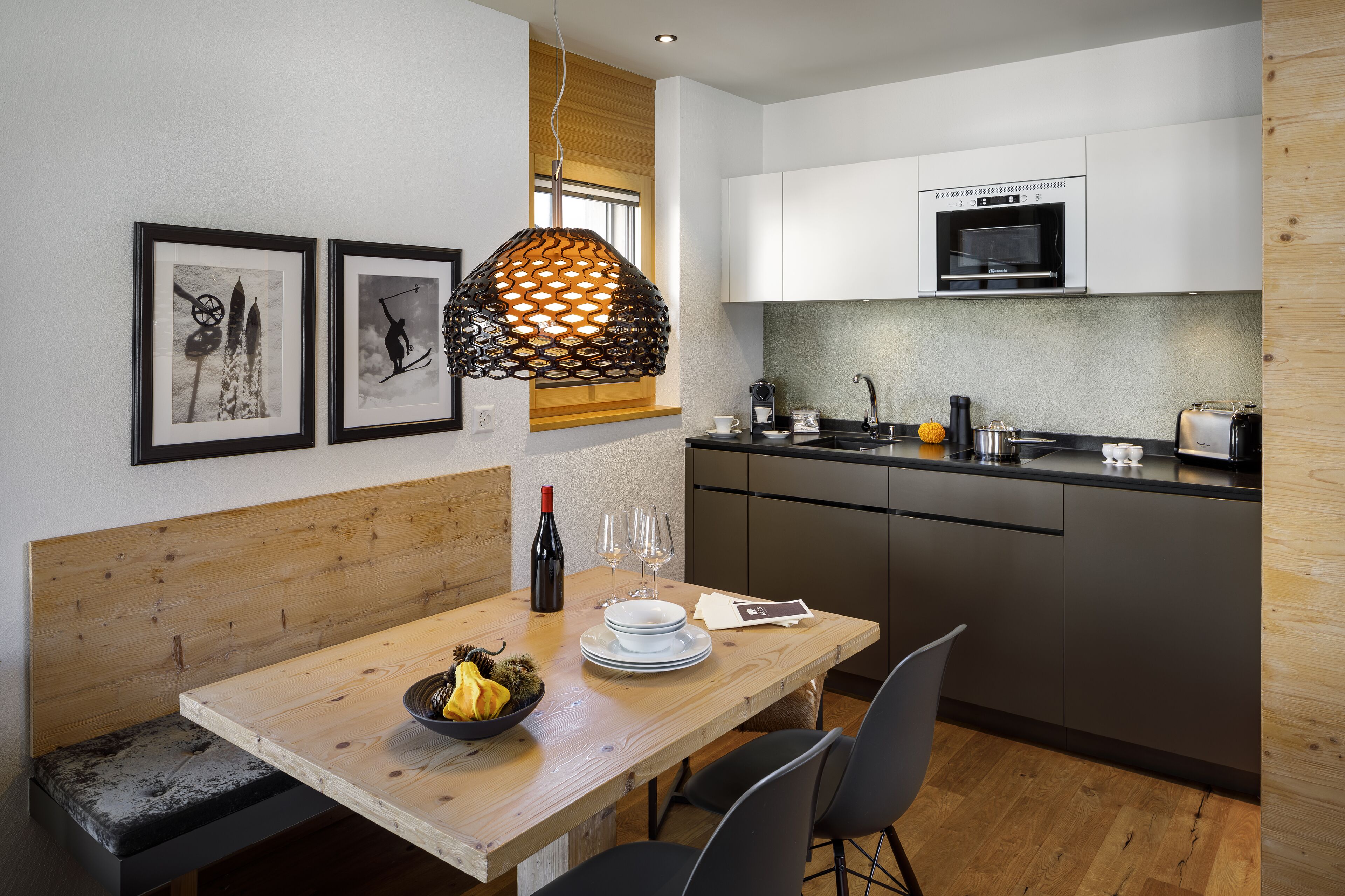 A modern kitchen with white cabinets, a built-in oven, and a dining area with a wooden table and chairs.