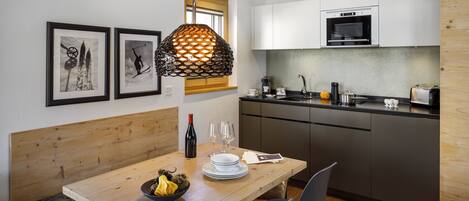 A modern kitchen with white cabinets, a built-in oven, and a dining area with a wooden table and chairs.