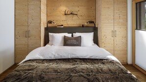Un dormitorio con cabecera de madera, ropa de cama blanca, un manto de piel y una decoración de cuernos montados.