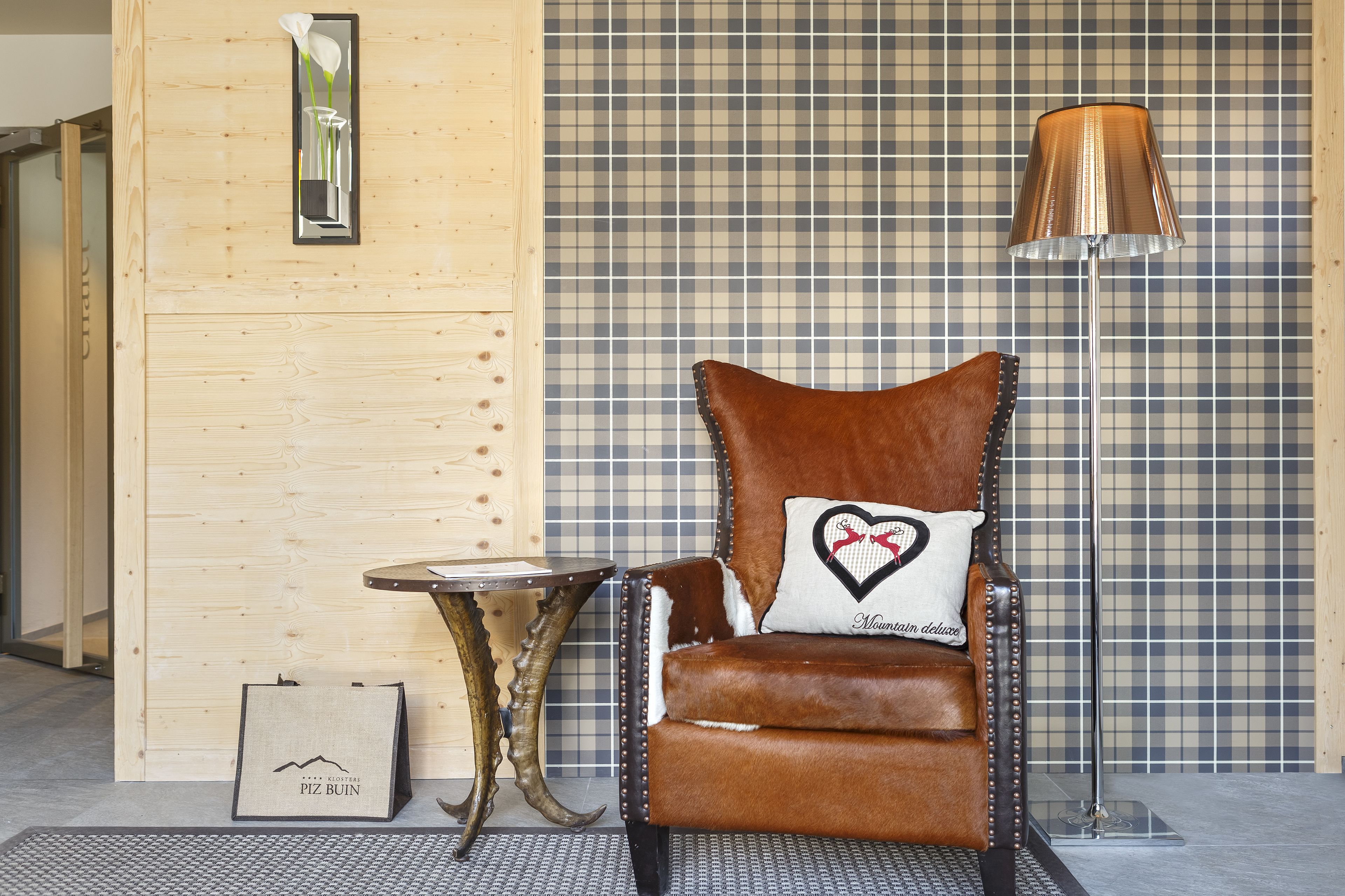 Un fauteuil en cuir marron agrémenté d’un coussin en forme de cœur, une petite table, une lampe et un mur en bois orné d’un motif à carreaux.